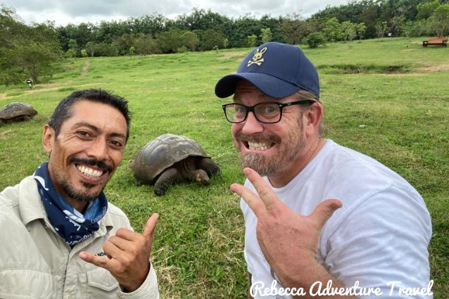Traveler and his guide posing in front of a giant Galapagos tortoise