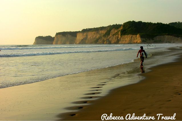 Surfer walking down Ayampe beach, one of the best destinations to go surfing and camping 